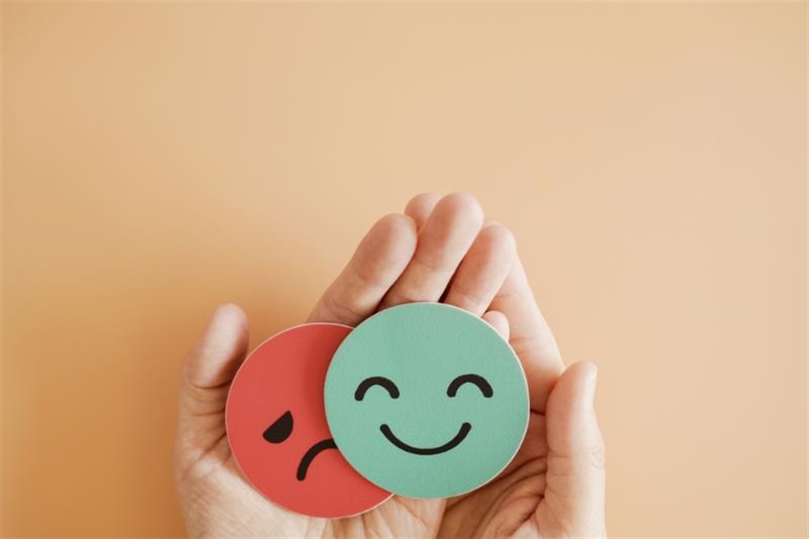 Hands holding wooden happy and sad faces