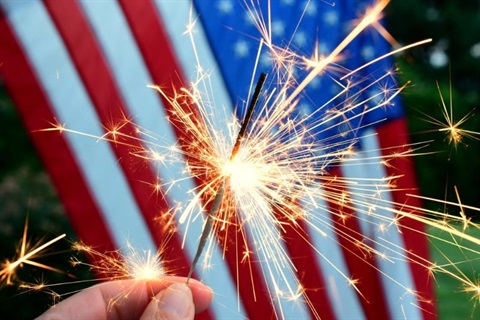 hand holding sparkler in front of American flag