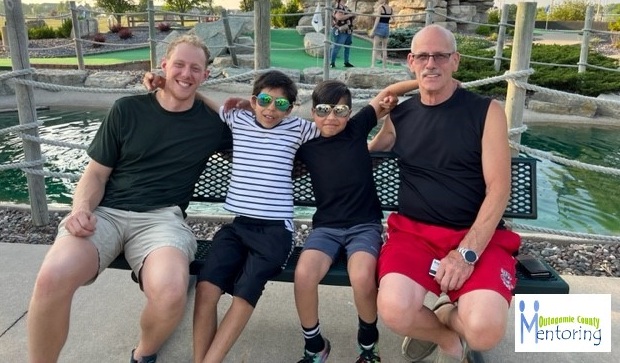 Adult male mentors and two boys sitting together on a bench at a mini golf park